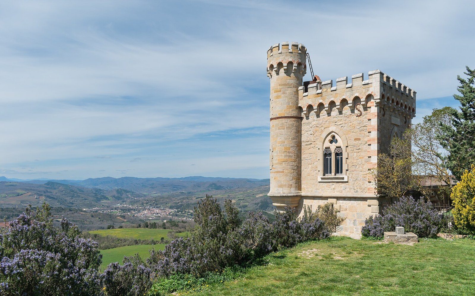 Crenellated stone tower overlooks a valley with distant hills and hazy sky